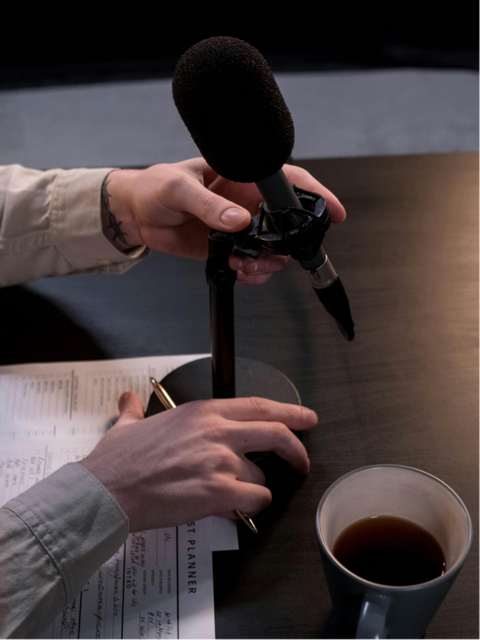 condenser microphone on a desk stand, with audio equipment blurred in the background