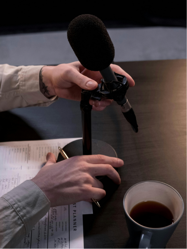 condenser microphone on a desk stand, with audio equipment blurred in the background
