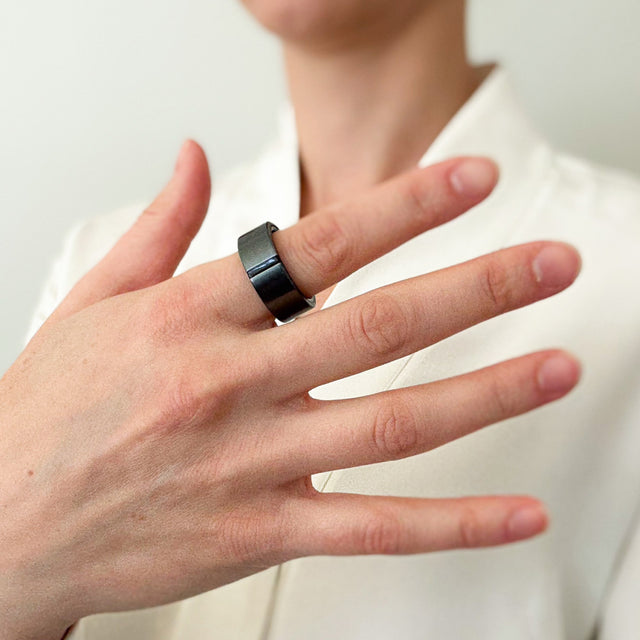 Hand wearing a graphite Lotus ring on the index finger against a white background.