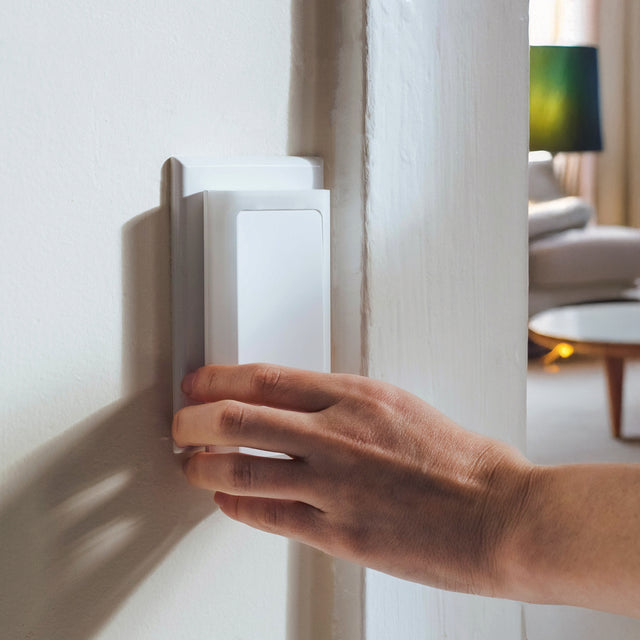 A person's hand is shown placing a white switch cover on a wall switch.