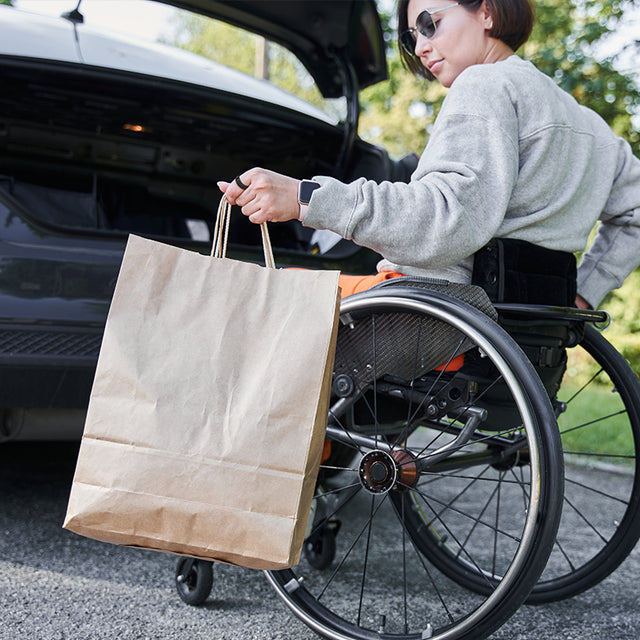 Woman in a wheelchair loading a shopping bag into the car trunk